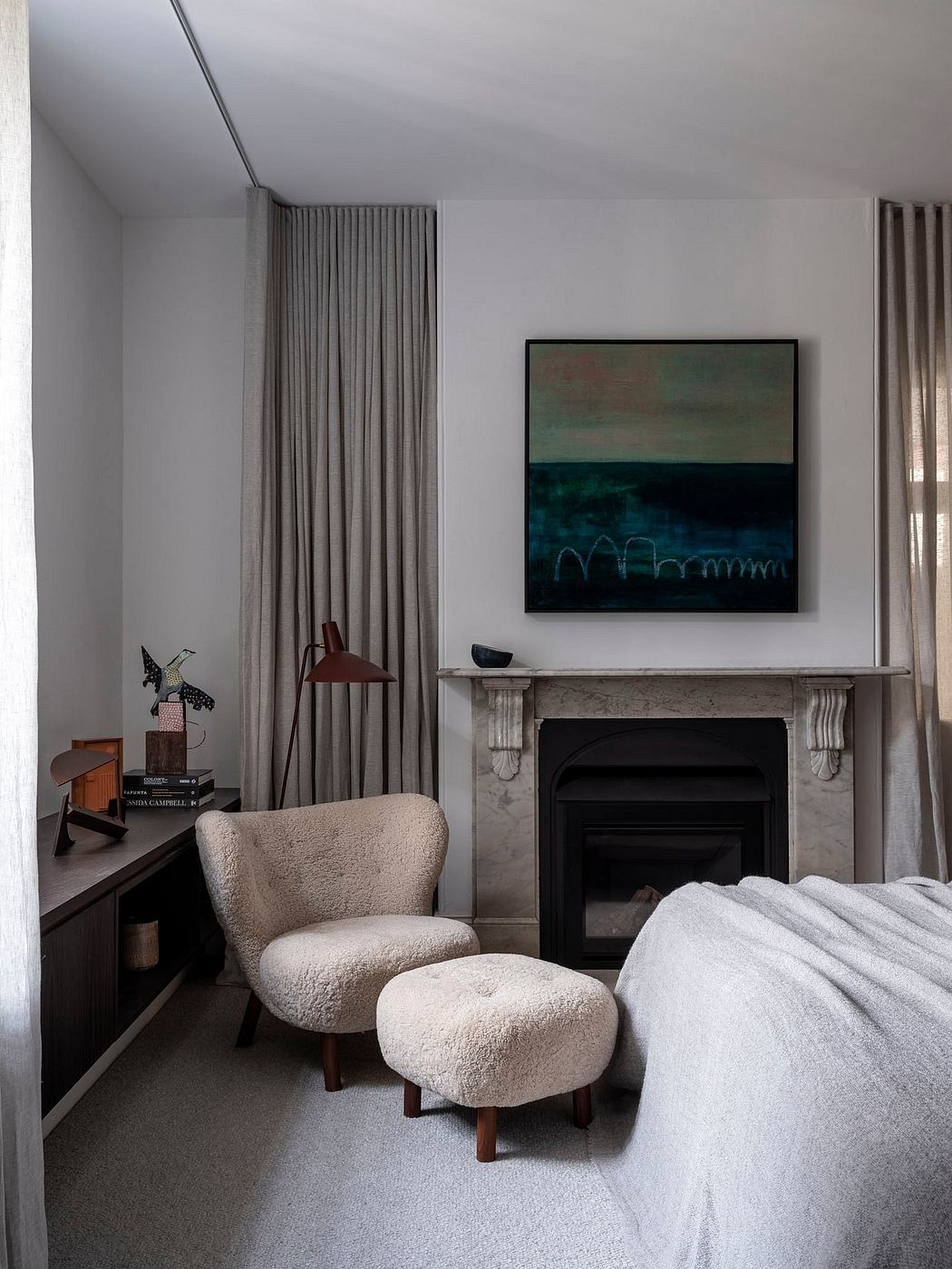 Cozy bedroom with plush chair, art piece, and fireplace in minimalist decor.