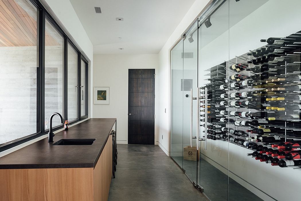 Minimalist kitchen with sleek black countertop, glass wine cellar, and modern decor.