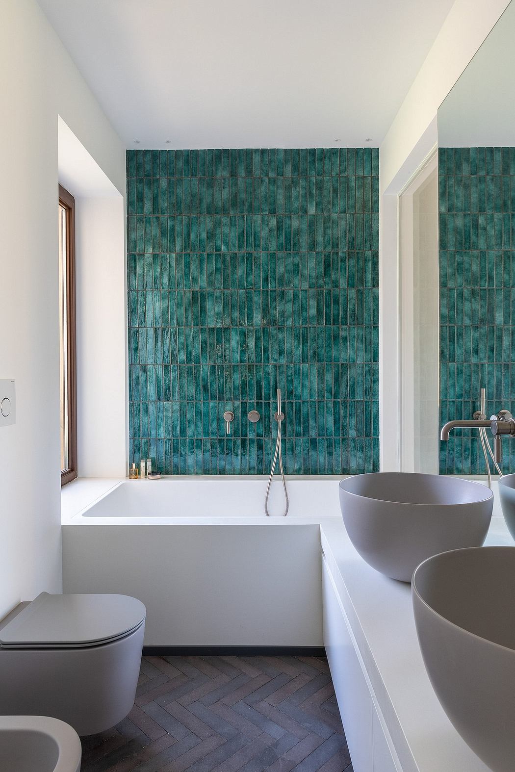 Minimalist bathroom with teal tile wall, white fixtures, and herringbone floor tiles.