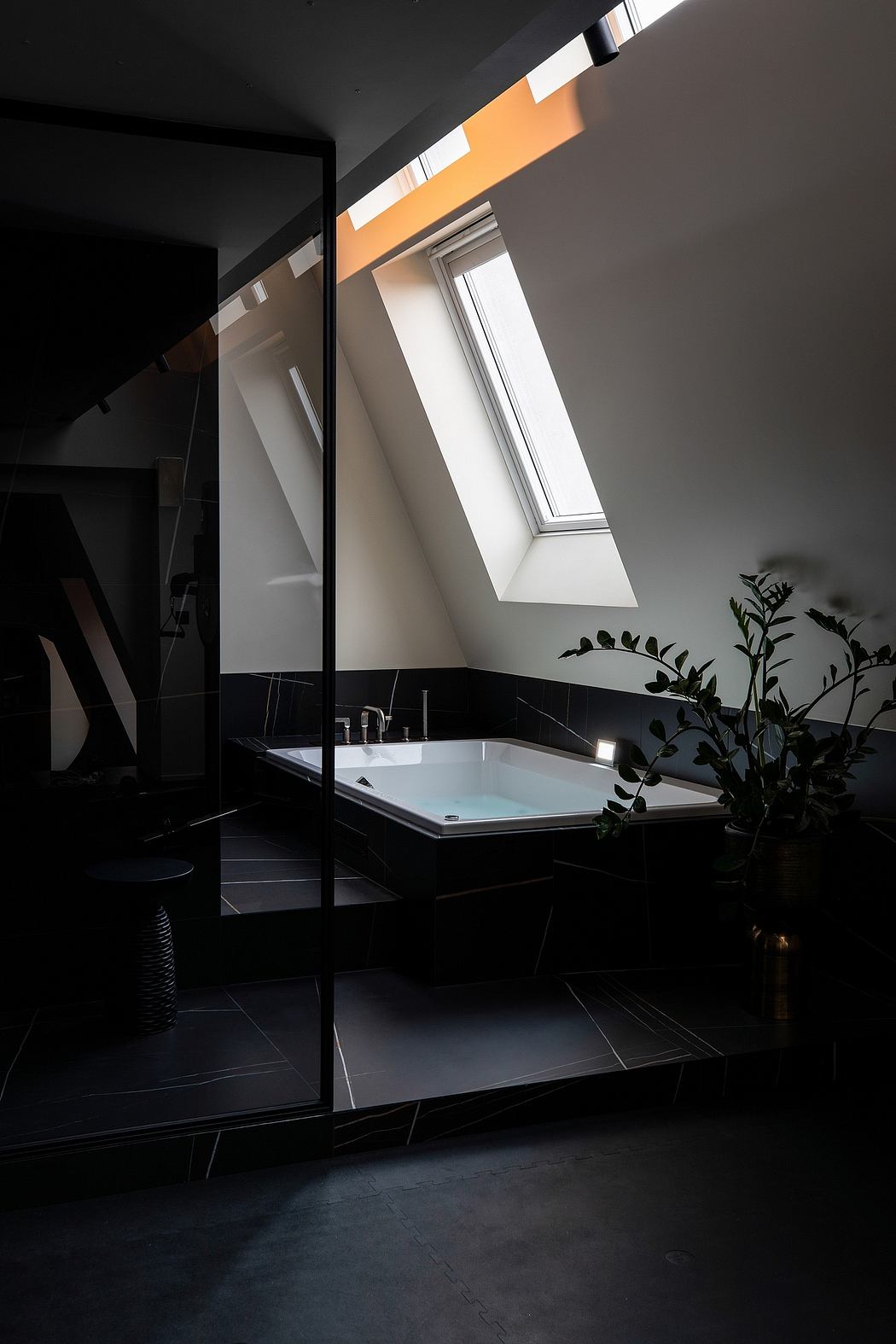 A modern bathroom with a skylight, sleek black tiles, and a freestanding bathtub.