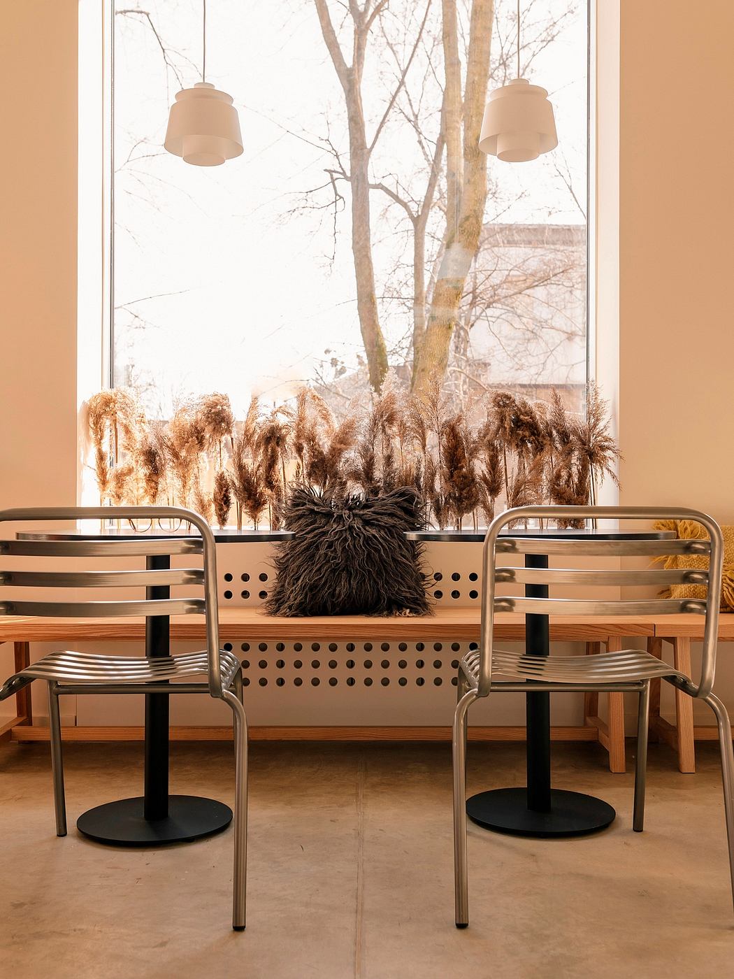 Cozy seating area with sleek metal chairs, plush pillow, and pampas grass decor framing the window.