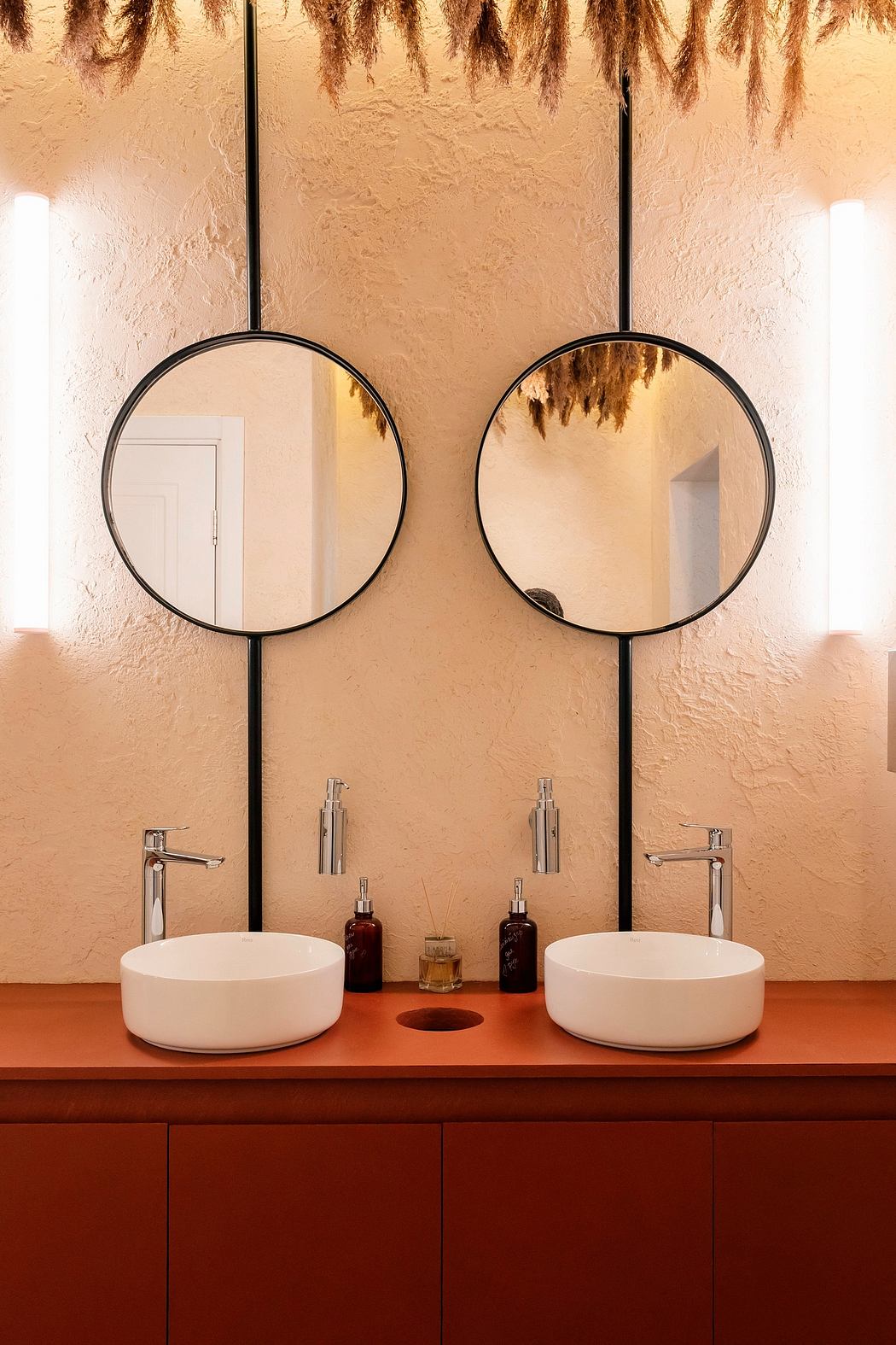 Modern vanity with circular mirrors, floating sinks, and hanging pampas grass.