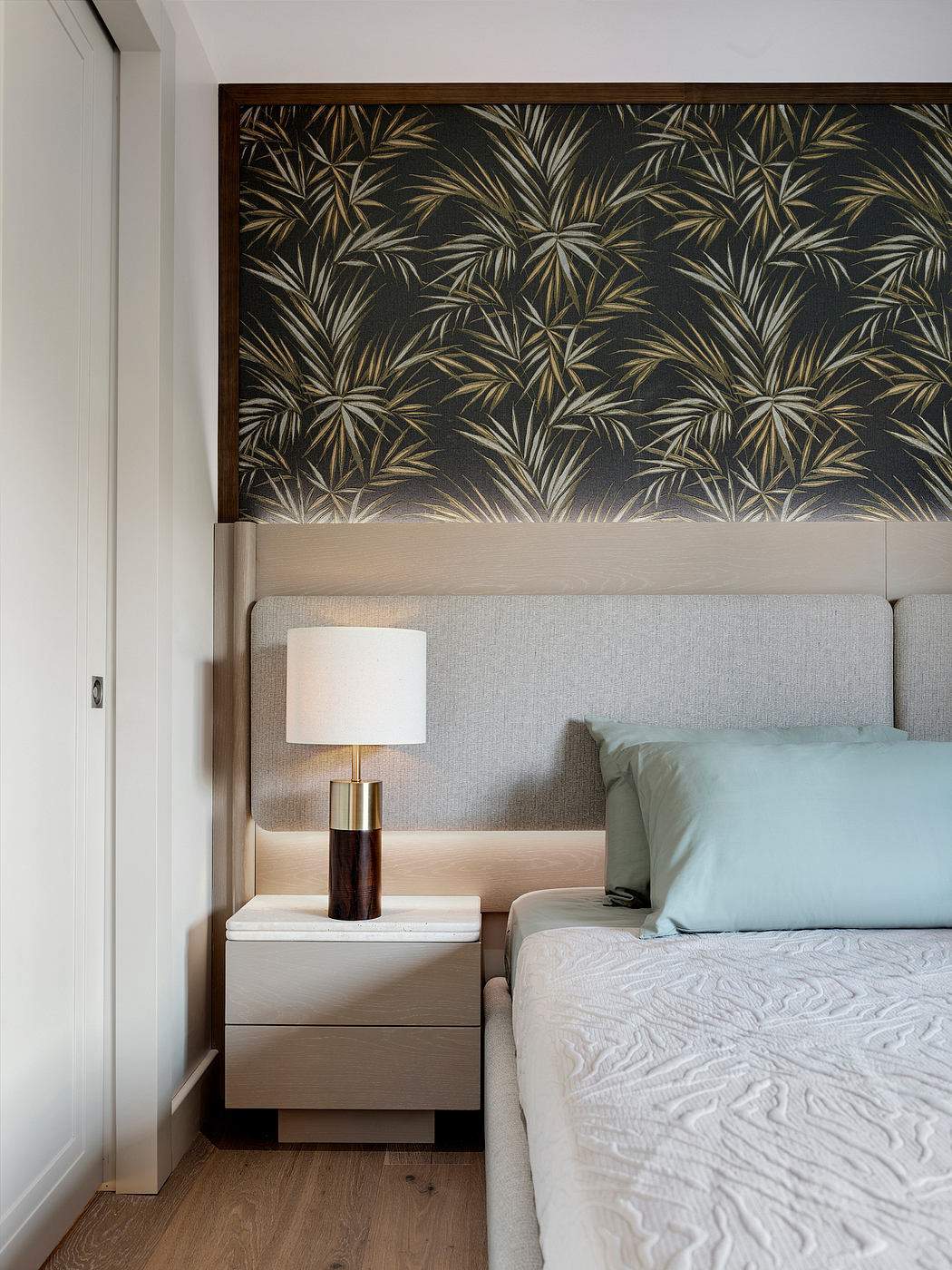 Minimalist bedroom with dark tropical botanical wall panel, nightstand, and soft textures.