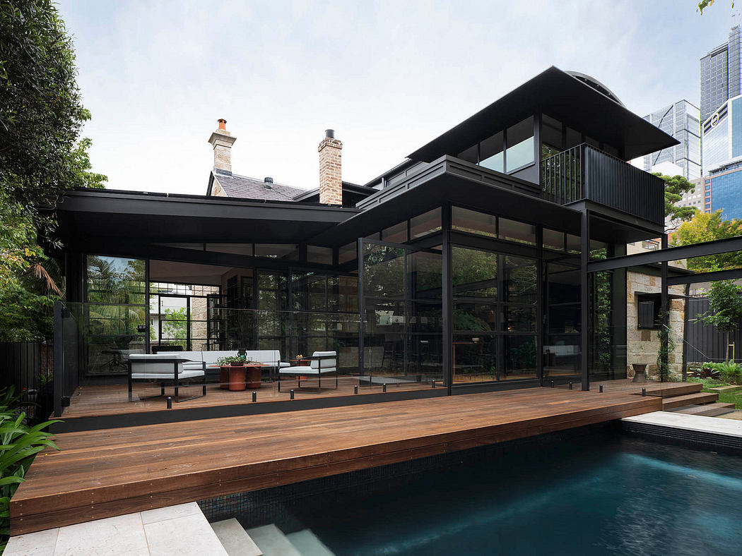 Contemporary glass and steel structure with wooden deck and pool, surrounded by foliage.