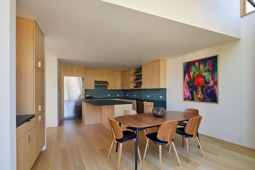Modern kitchen and dining area with wooden cabinets, black countertops, and colorful artwork.
