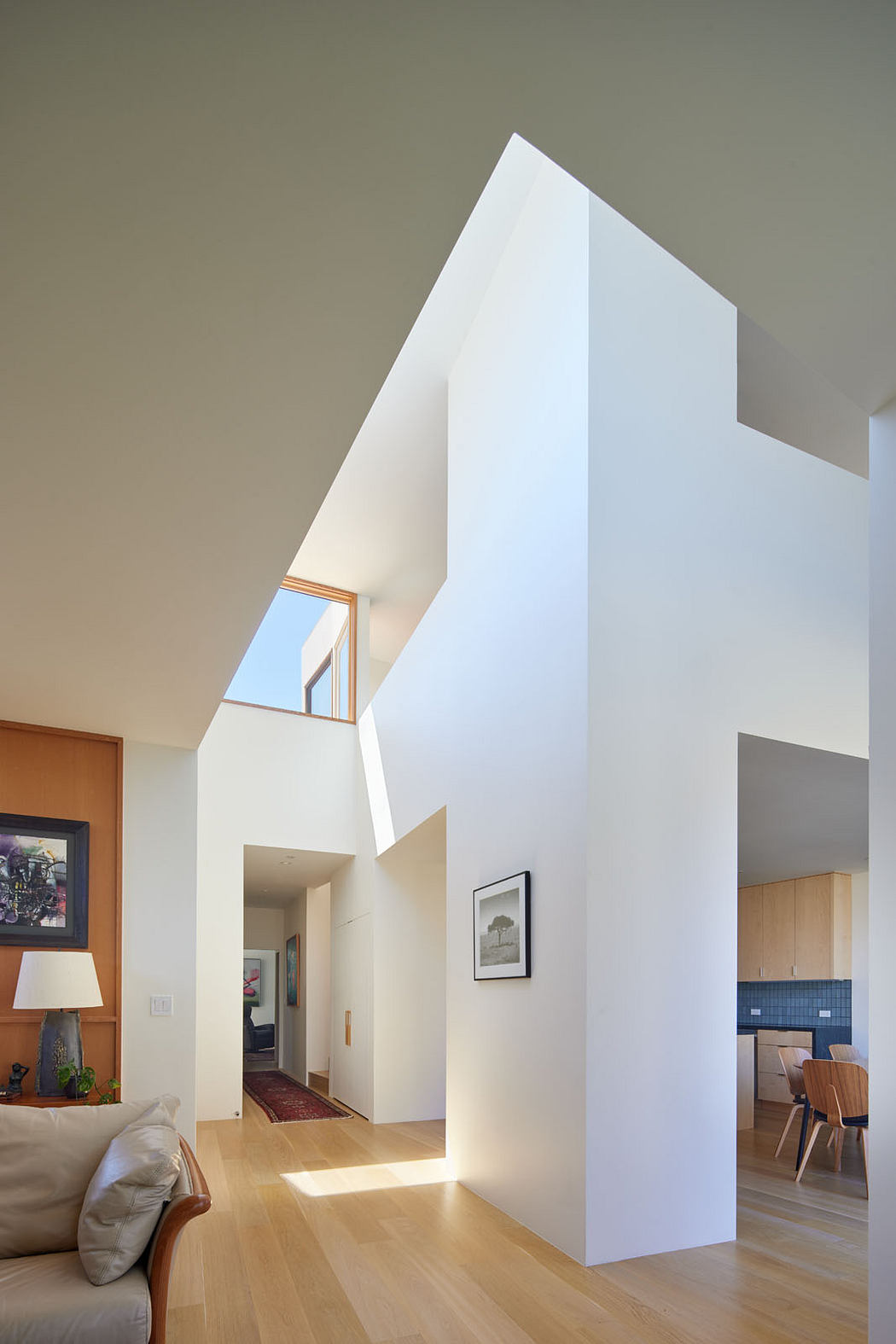 Modern, open-plan interior with angular architectural features, wood flooring, and artwork.