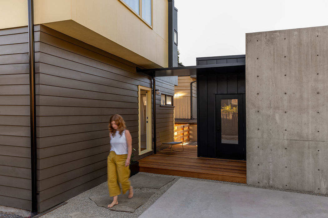 The image depicts a modern, minimalist architectural design with a wooden exterior, concrete walls, and a recessed entryway.