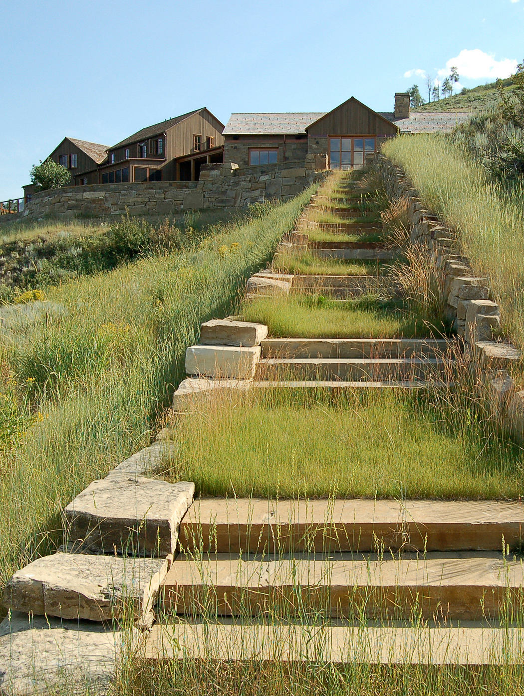 A rustic wooden cabin nestled atop a stone-stepped hillside, surrounded by lush greenery.