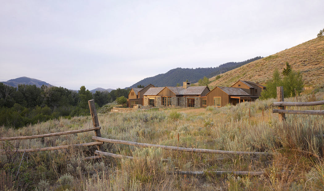 A rustic ranch with wooden structures and a fence nestled in a scenic mountainous landscape.