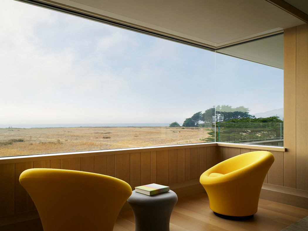 Warm, minimalist room with panoramic window overlooking rural landscape and yellow armchairs.