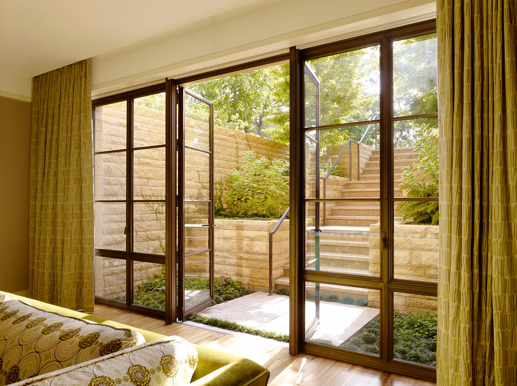 A cozy bedroom with large windows overlooking a lush outdoor garden and staircase.