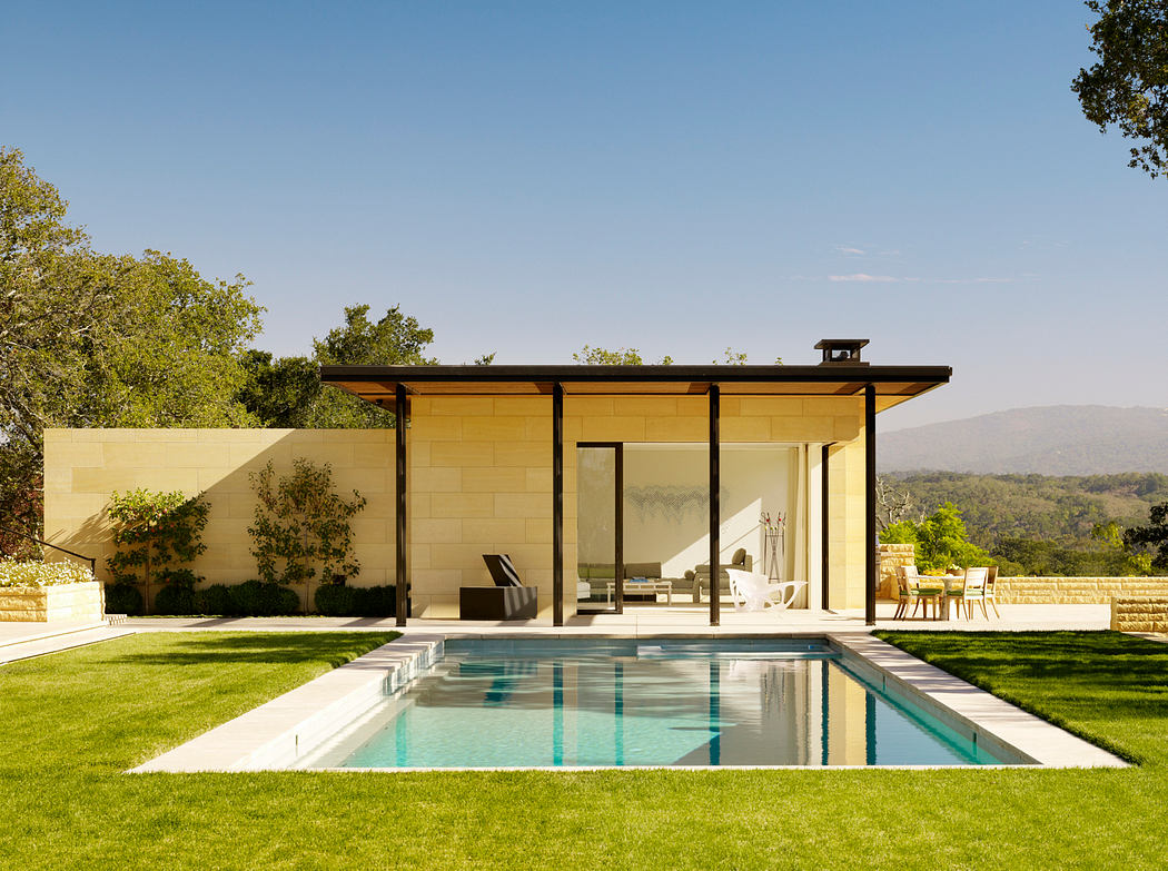 A modern, open-concept home with a sleek, glass-walled pool pavilion set against scenic hills.