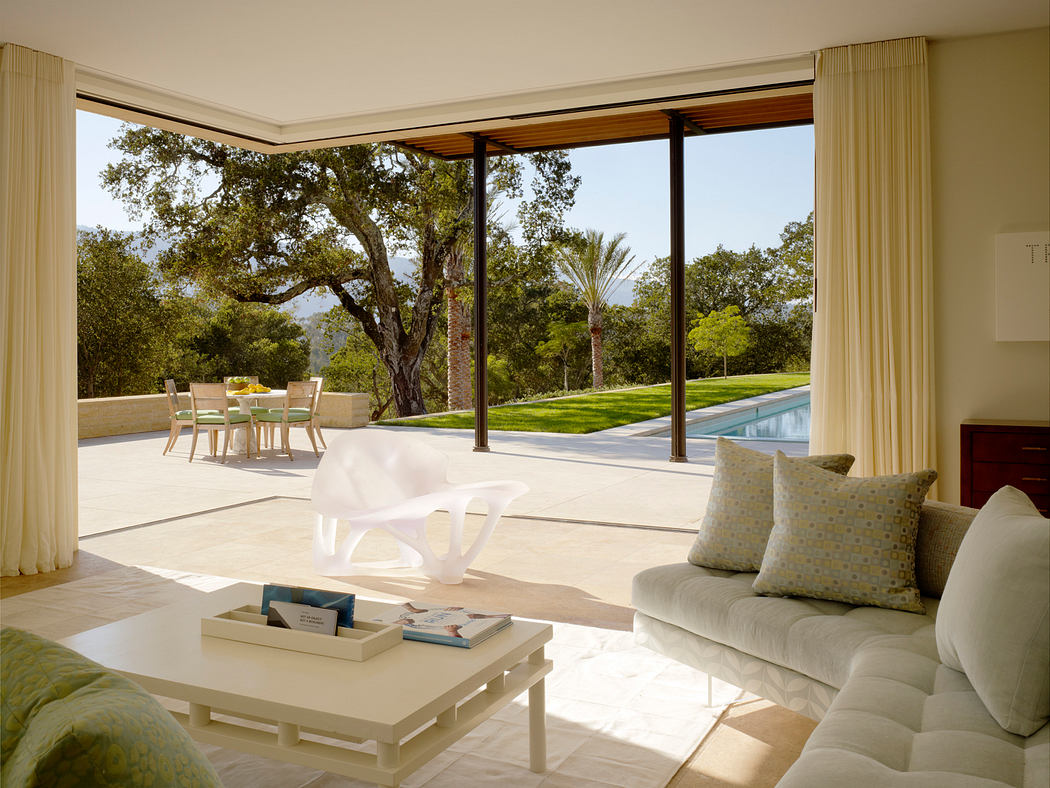 Airy living room with floor-to-ceiling windows overlooking lush, manicured garden and pool.