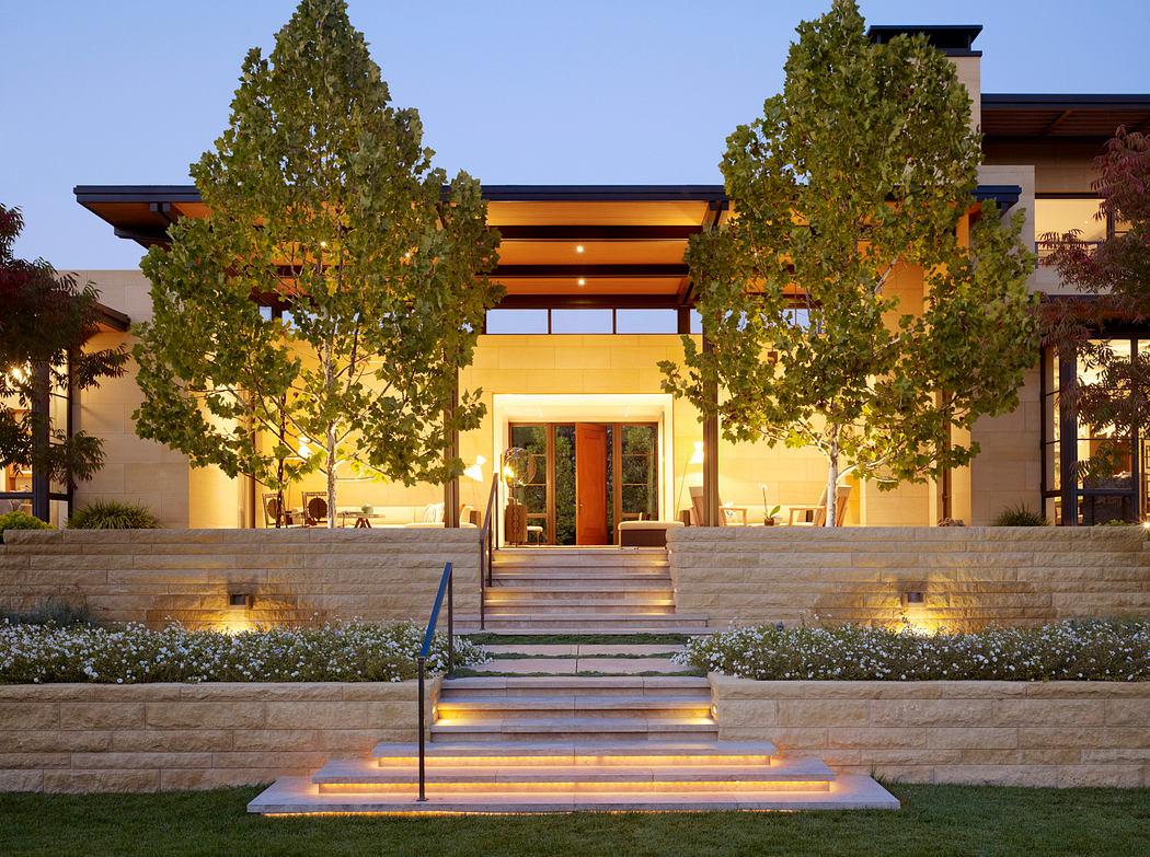 A modern, well-lit building with a warm, inviting entryway surrounded by lush greenery.