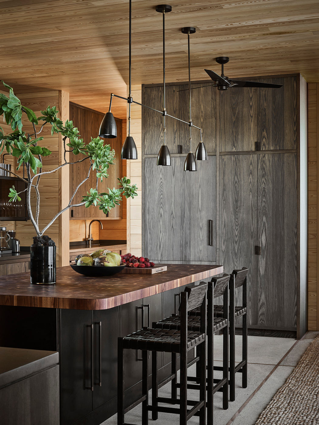 Rustic wood-paneled kitchen with sleek black cabinets, pendant lights, and a central island.
