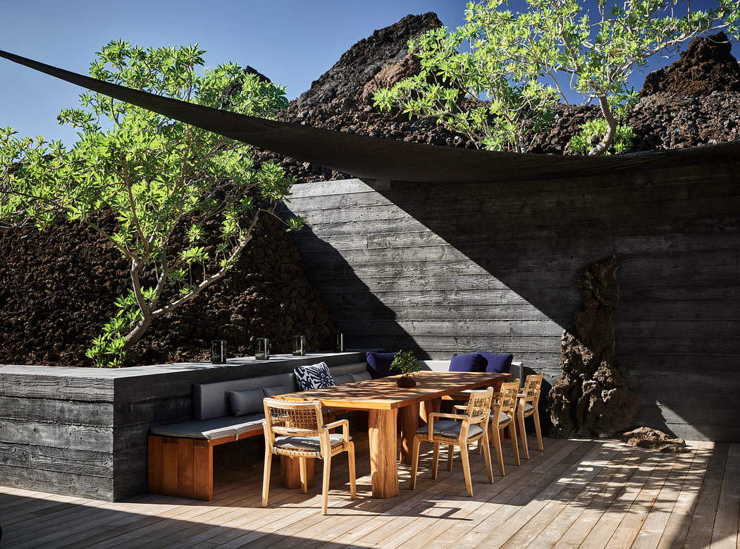 Rustic outdoor dining area with wooden furniture, stone walls, and lush greenery.