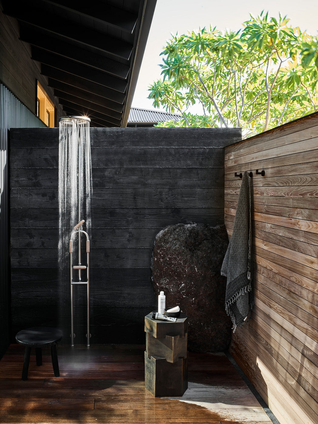 A rustic outdoor shower with a wooden structure, stone accents, and lush greenery.