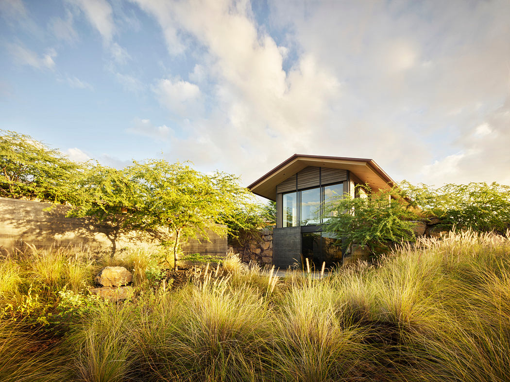 A modern, glass-walled house nestled among lush tropical foliage and grassy meadows.