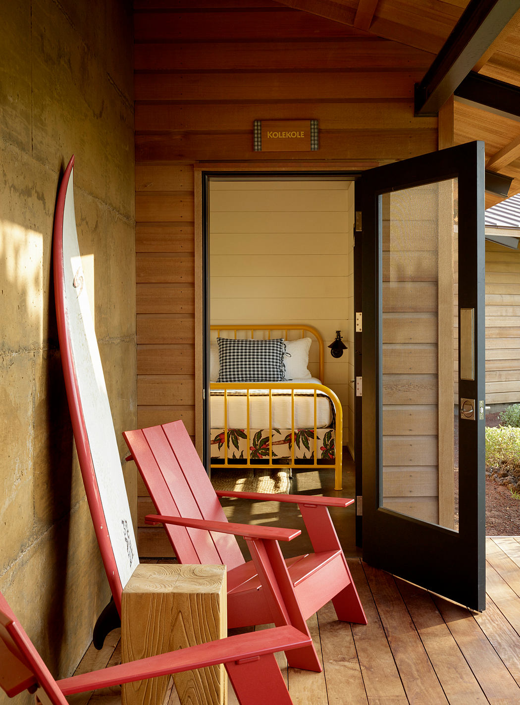 Rustic cabin with wooden walls, Adirondack chairs, and a cozy bedroom visible through the open doorway.