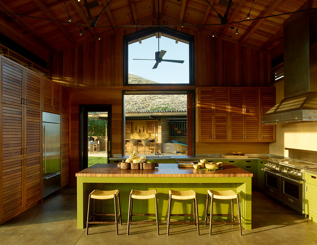 Rustic kitchen with wooden cabinetry, green island, and large arched window revealing outdoor views.