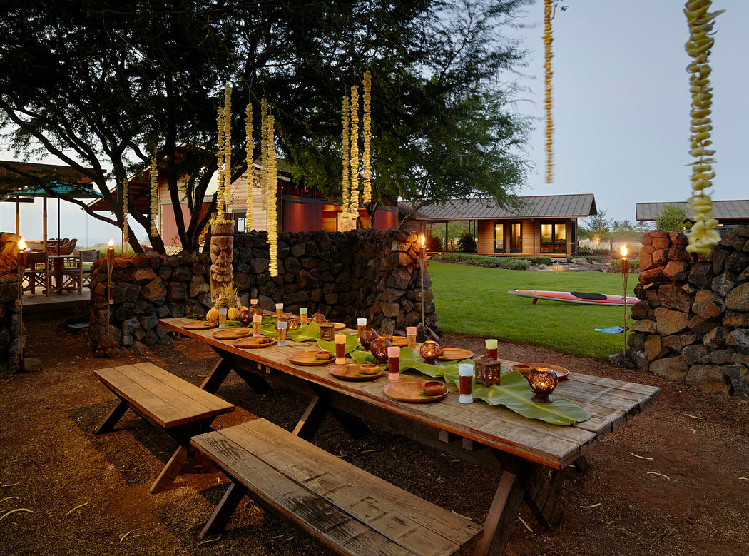 A rustic outdoor dining area with a stone wall, wooden table, and lush greenery around a cozy cabin.