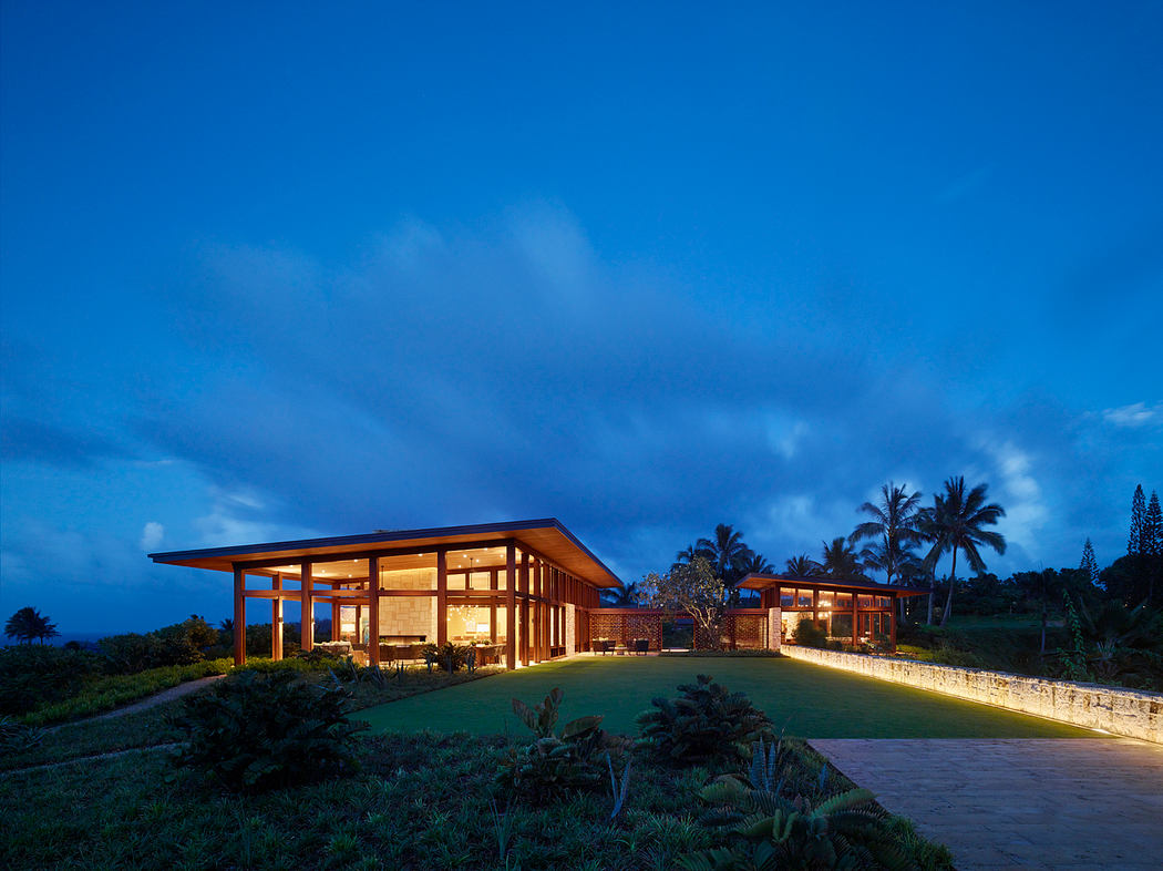 A modern, open-air tropical home with wooden beams, large windows, and lush landscaping.