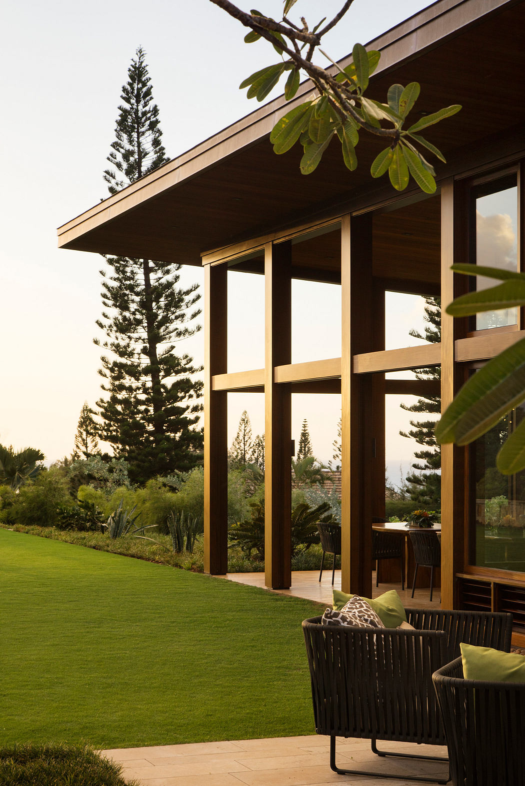 A modern, wooden-framed home with large windows overlooking a manicured lawn and lush greenery.