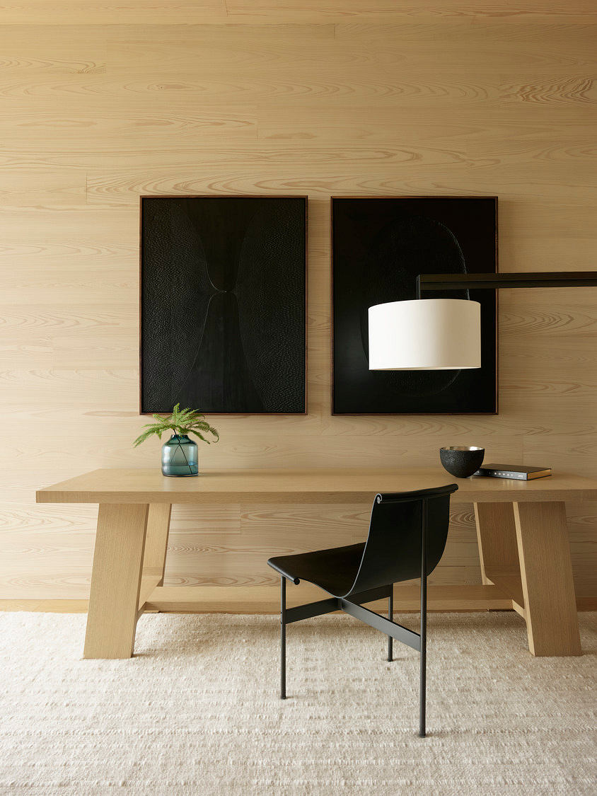 Minimalist workspace with wooden table, black chair, and framed artwork on the wall.