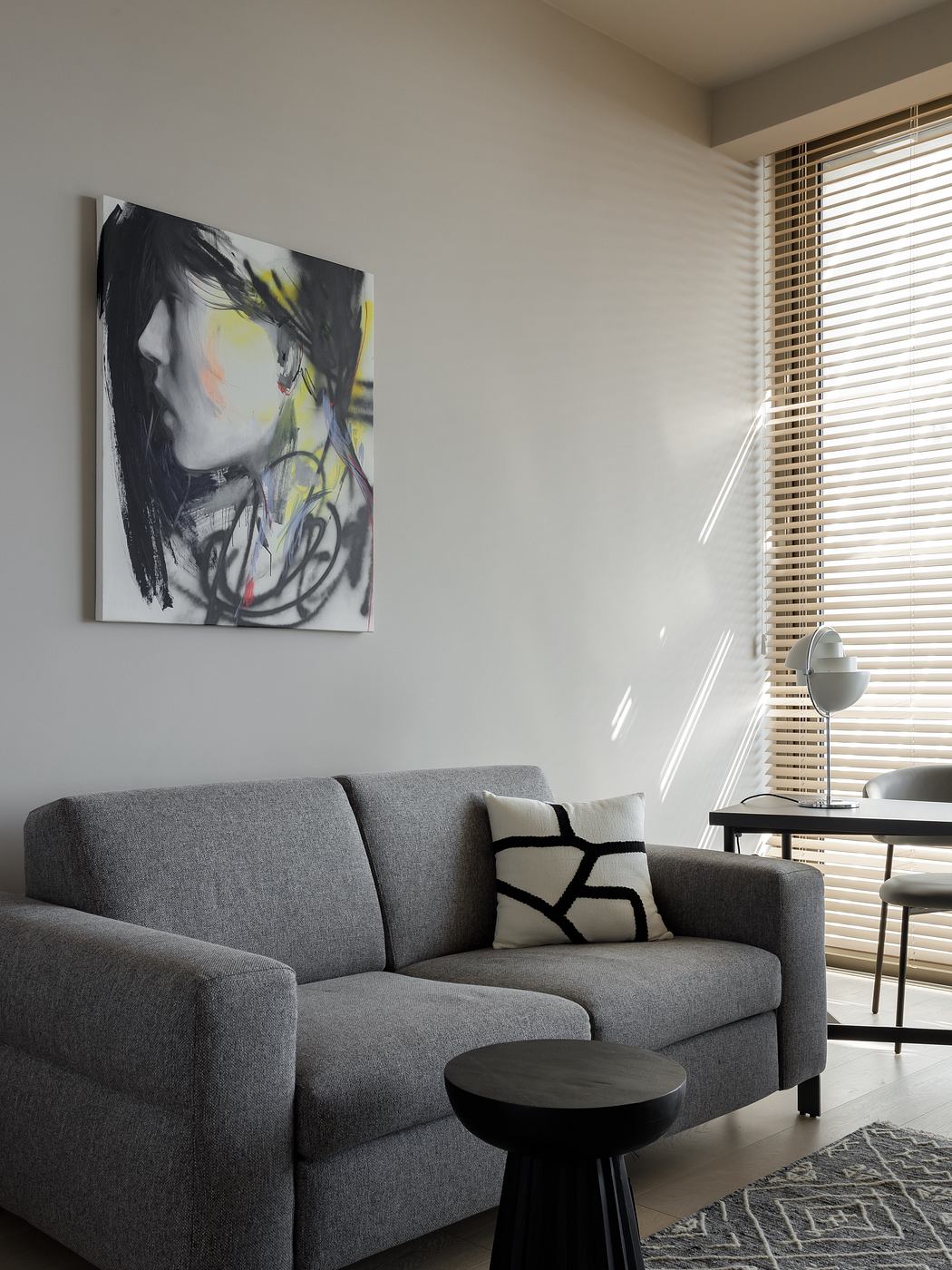 Modern, minimalist living room with abstract art, gray couch, and wood accent table.