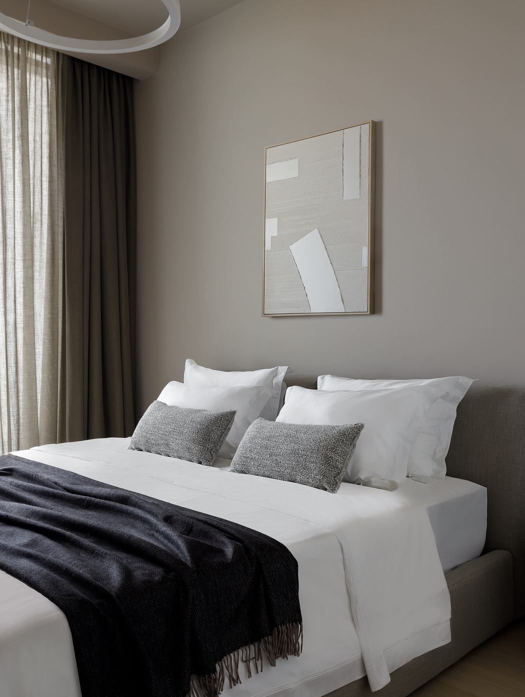 Clean, minimalist bedroom with neutral tones, abstract artwork, and textured pillows.