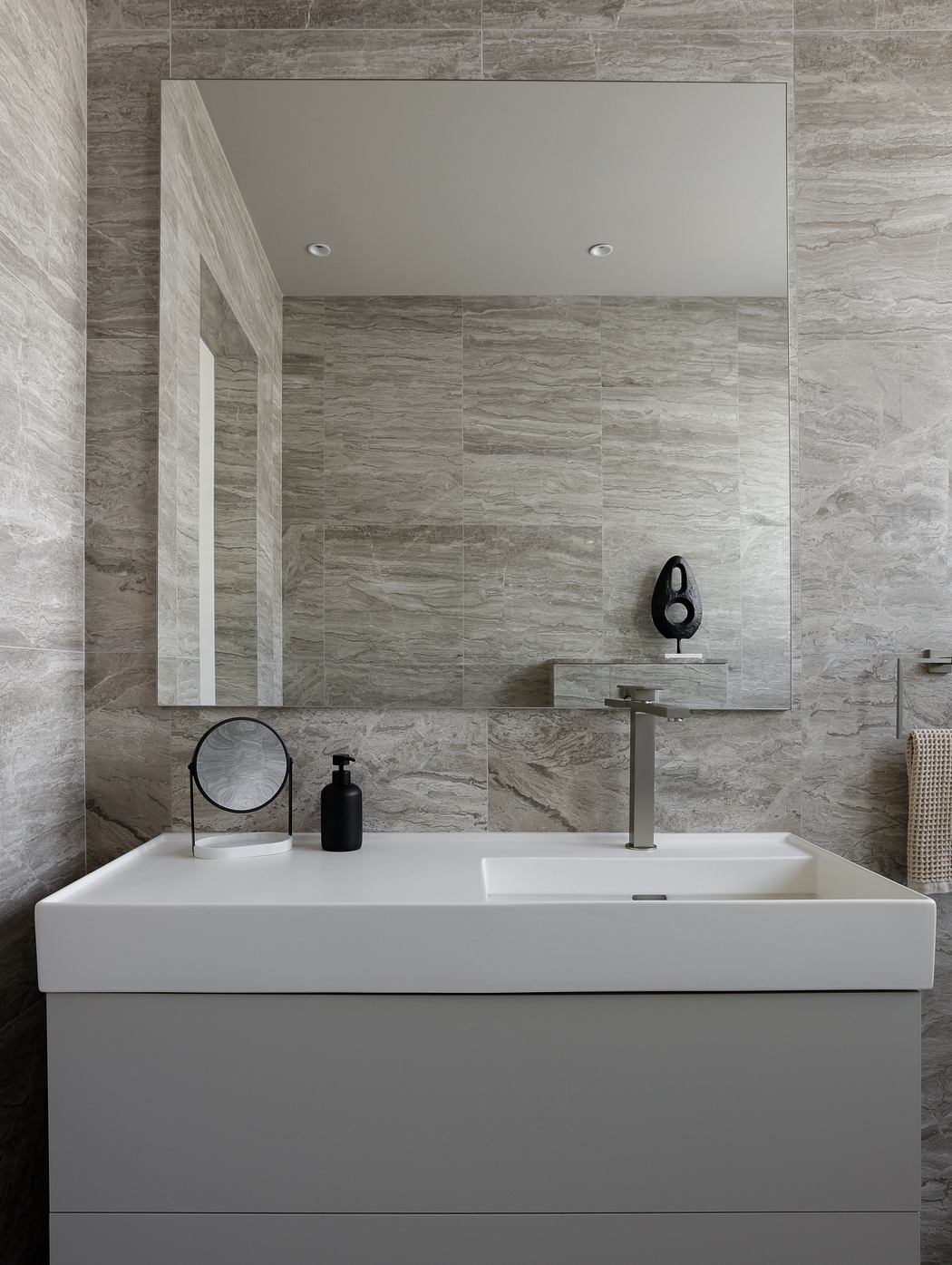 Sleek, minimalist bathroom design with grey stone wall tiles and a simple white sink.