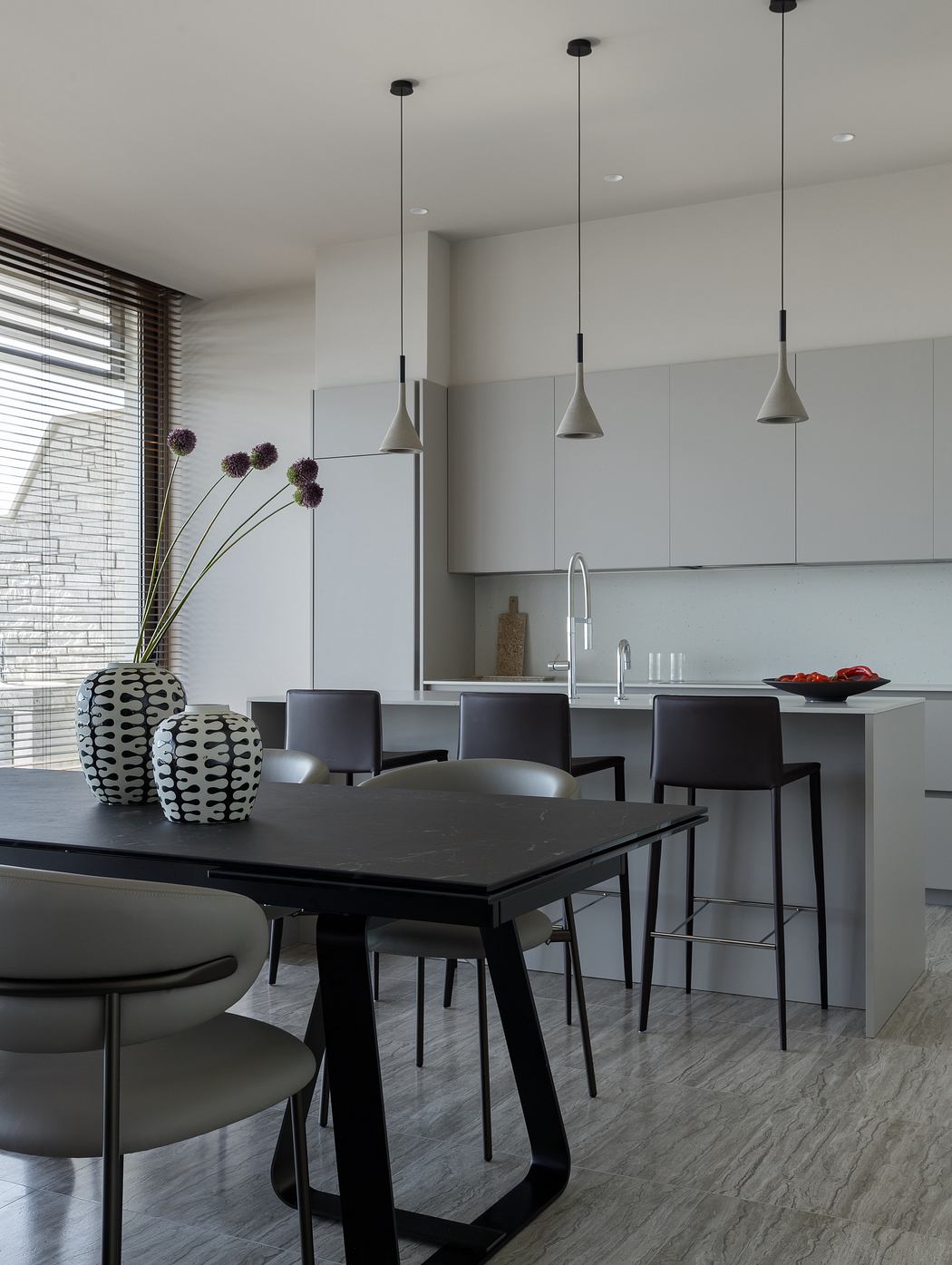 Modern kitchen and dining area with sleek black furniture, pendant lights, and marble floor.