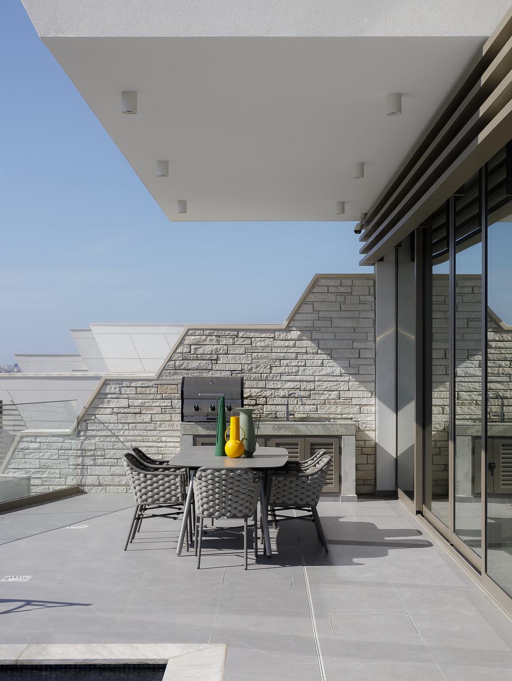 A modern outdoor patio with a stone wall, glass doors, and a dining table with contemporary chairs.