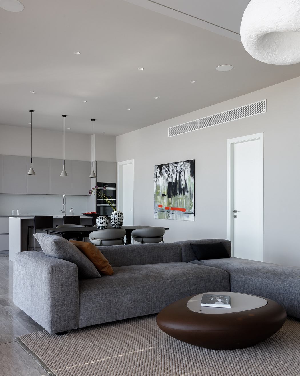 A modern, minimalist living room with a gray sectional, pendant lights, and an abstract artwork.