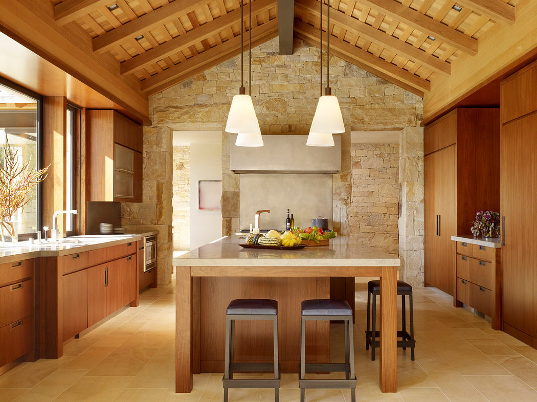 Rustic wooden beams, stone walls, and a large central kitchen island with pendant lighting.