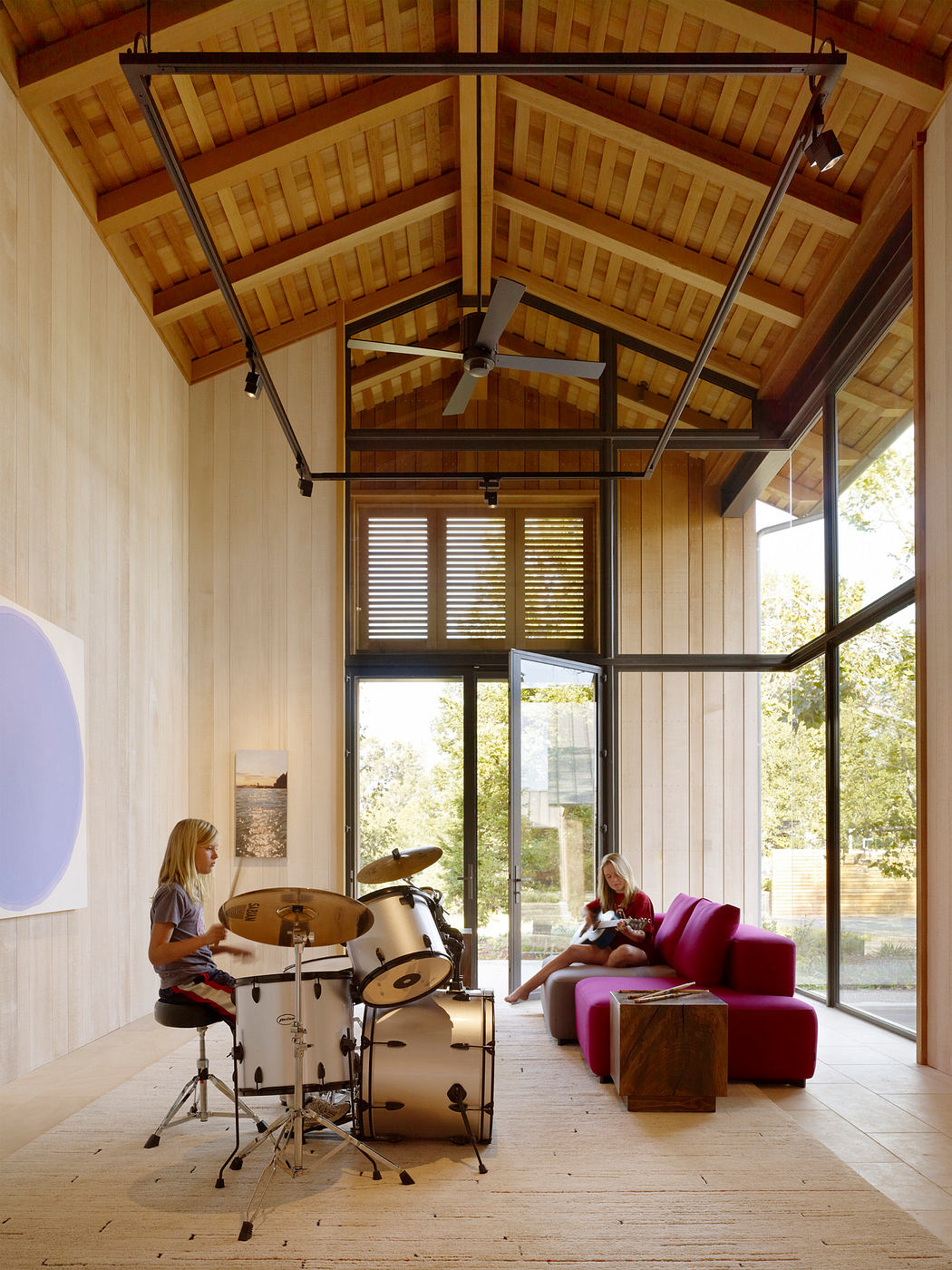 Wooden ceiling beams, large windows, and a modern drumset create a cozy, rustic atmosphere.