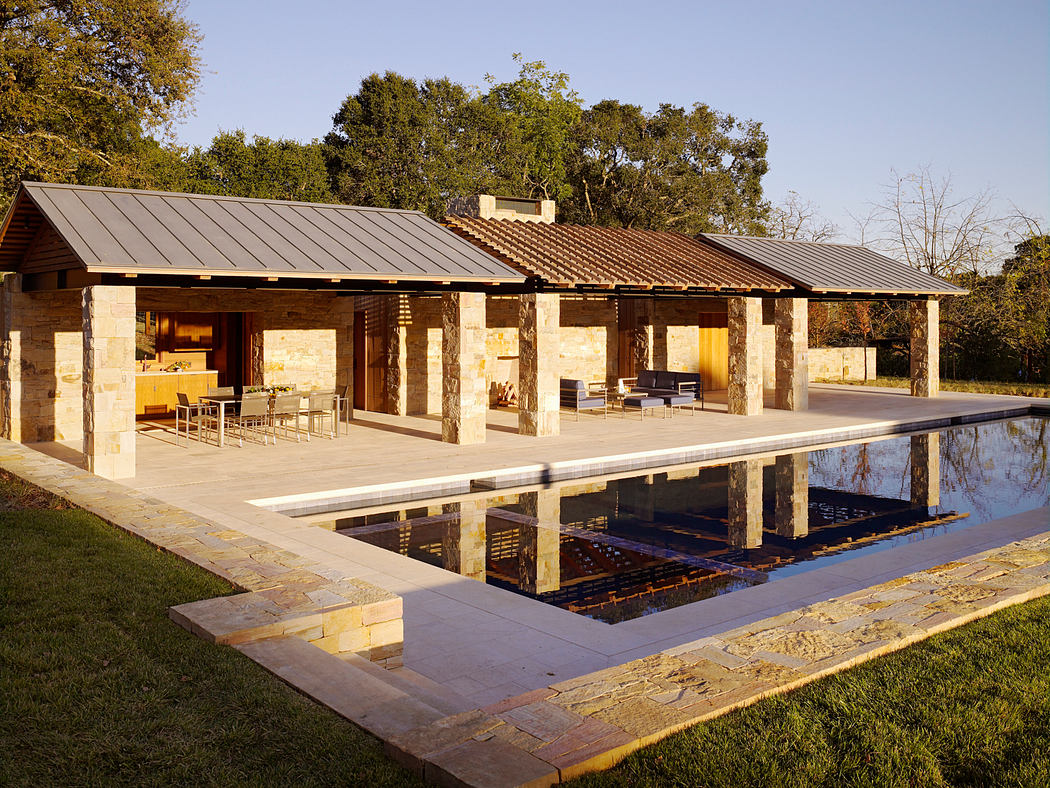 Rustic stone structure with sleek metal roof, surrounding pool, and patio seating.