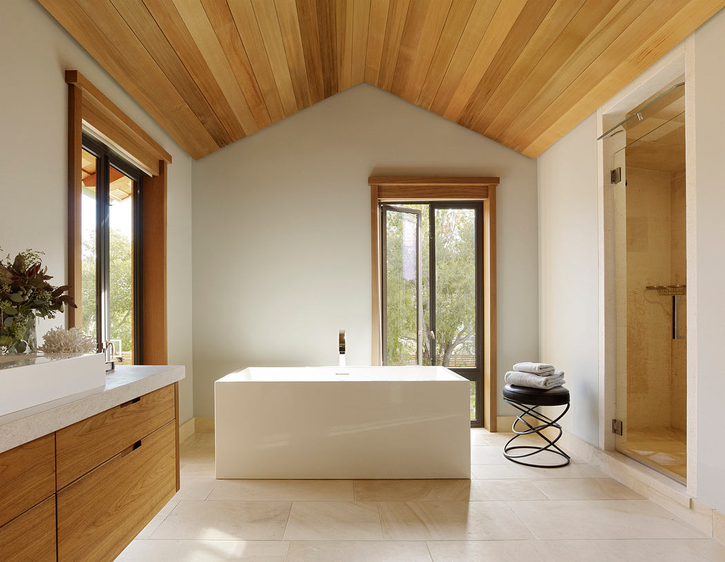 Spacious, modern bathroom with wood-paneled ceiling, large tub, and nature views.