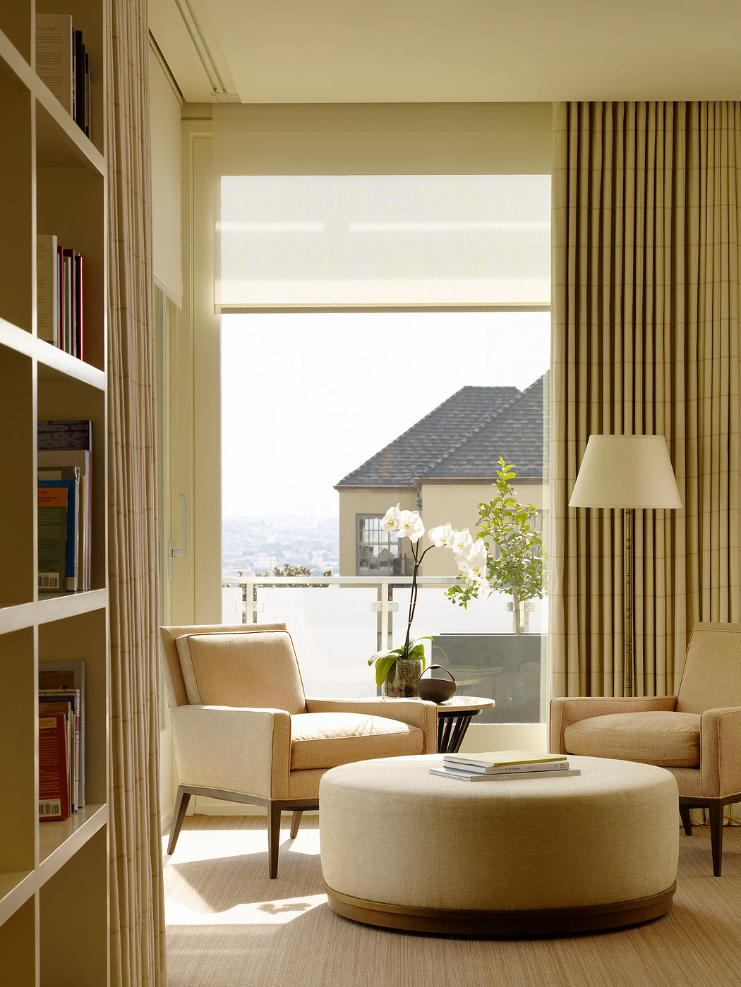 Cozy living room with plush armchairs, round ottoman, and floor-to-ceiling windows offering scenic city views.