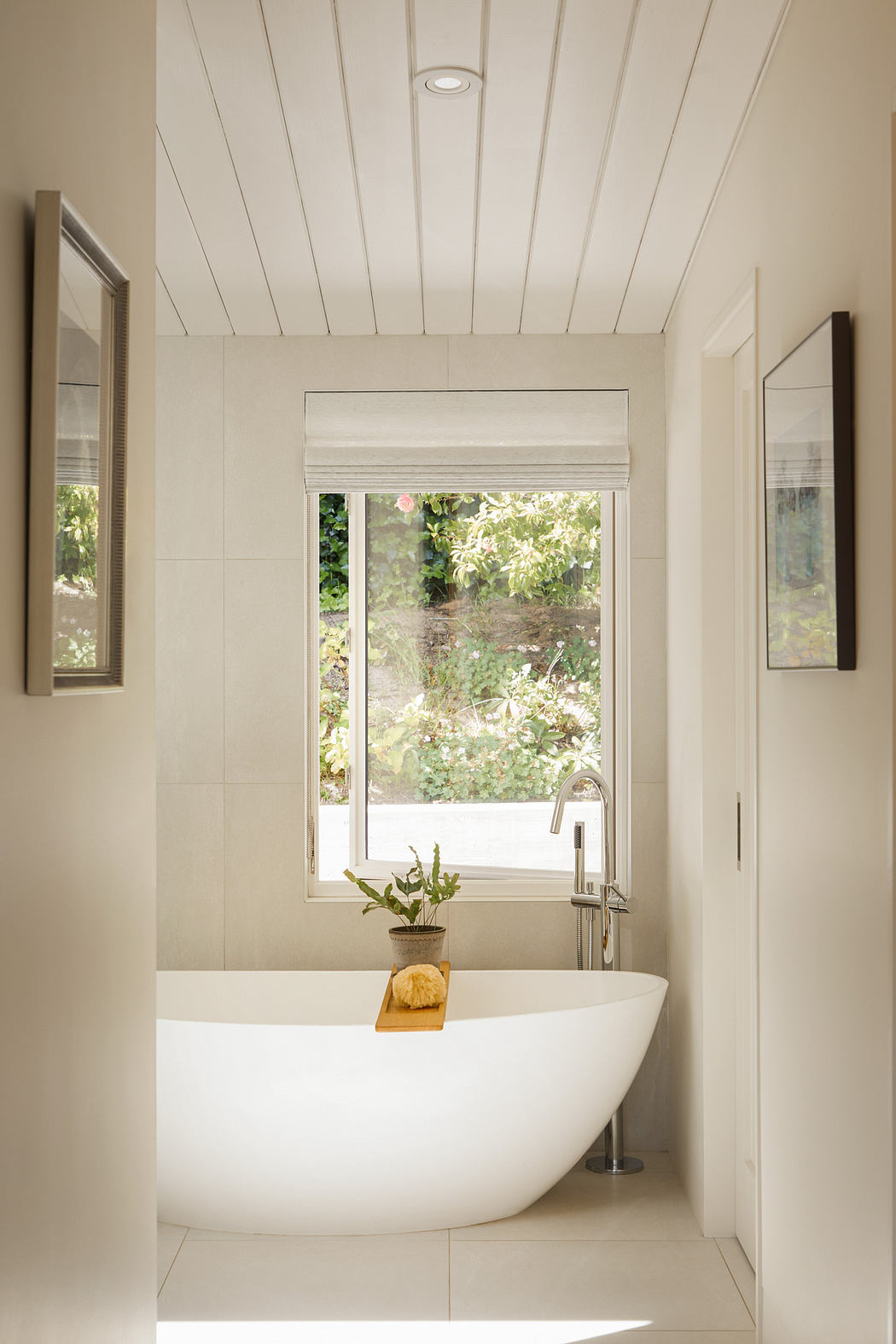 A serene bathroom with a white freestanding tub, large window, and a wooden decor accent.