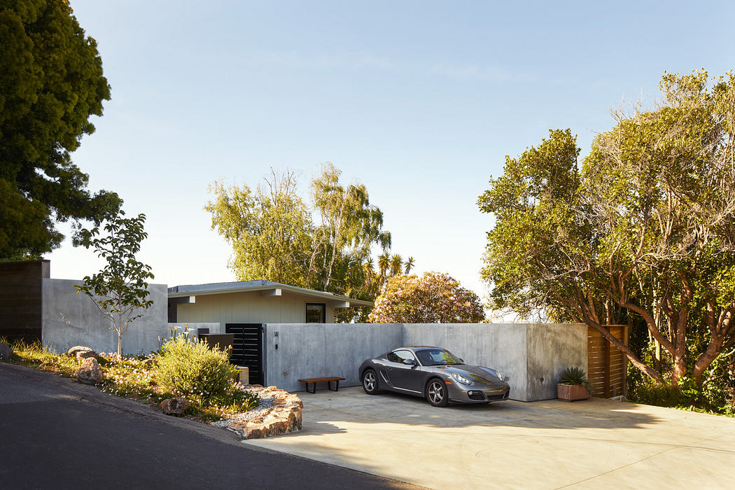 Modern two-story home with concrete exterior, gray Porsche sports car, and lush landscaping.