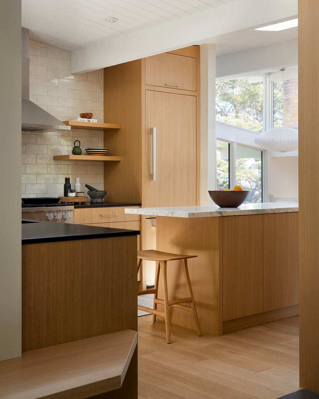 Modern kitchen with light wood cabinetry, marble countertops, and minimalist decor.