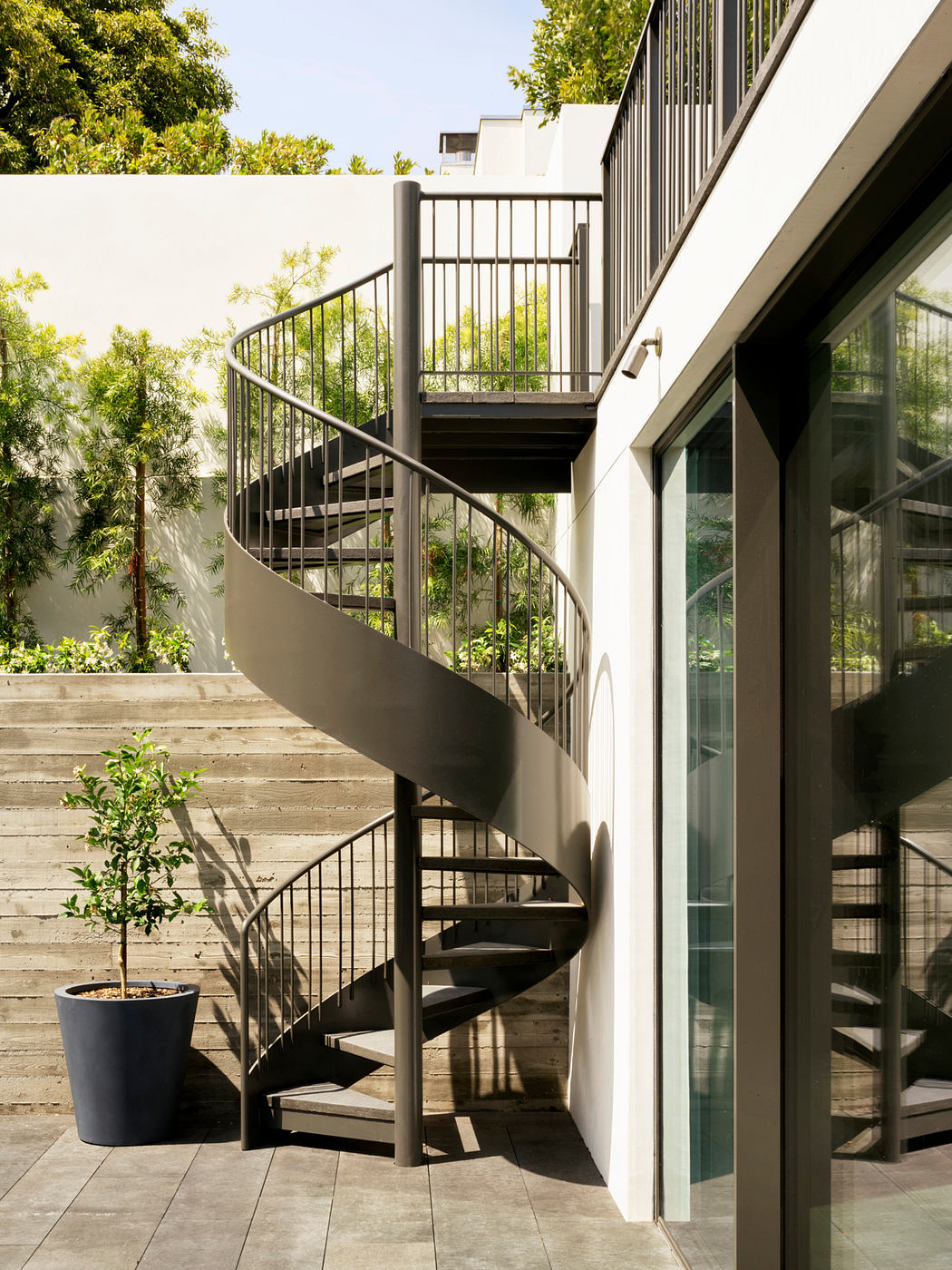 Spiral staircase, glass doors, and lush greenery create a modern, nature-inspired exterior.