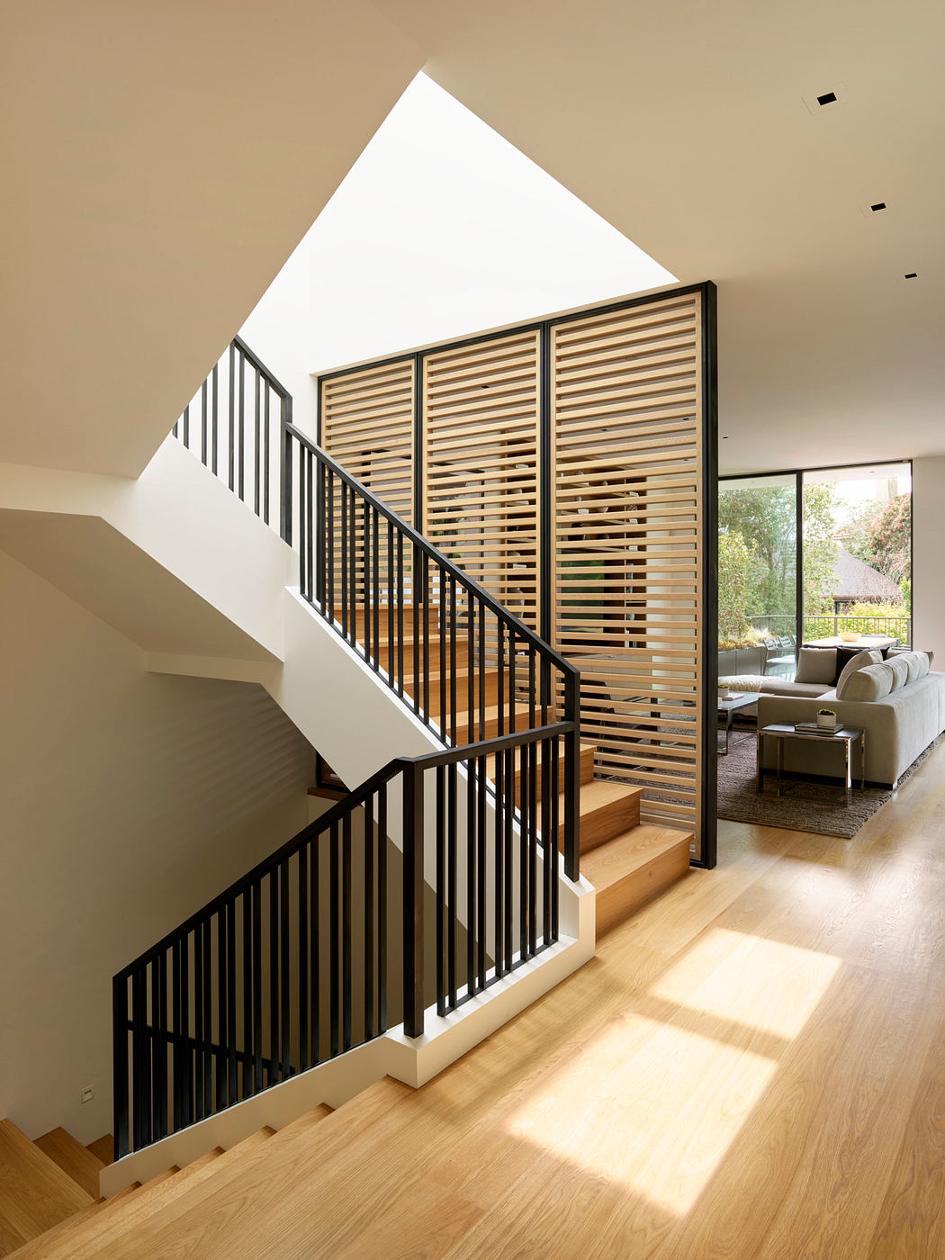 A modern staircase with wooden slats, metal railings, and a view of a cozy living room.