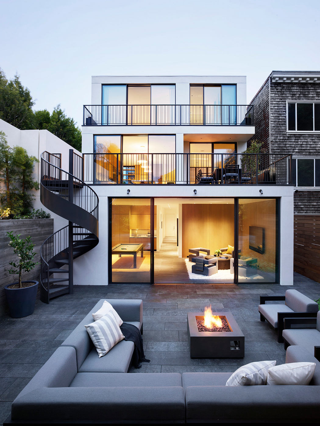 A modern, multi-level home with sleek, minimalist design, featuring glass walls, outdoor patio, and a stylish firepit.