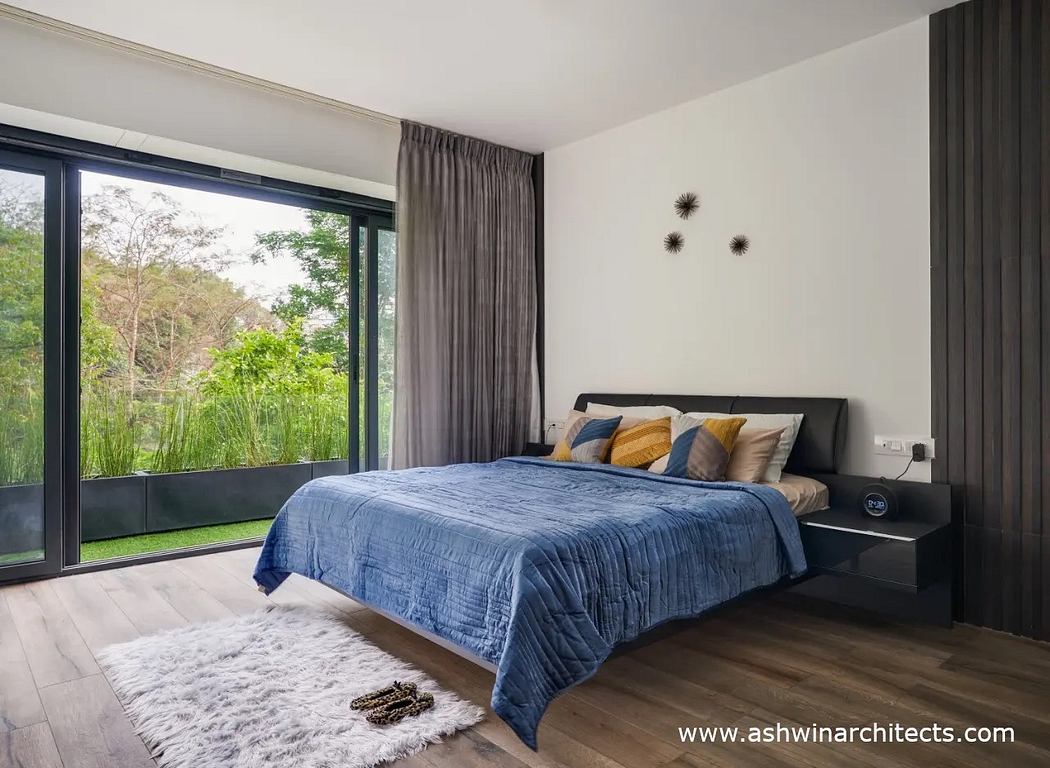 Modern bedroom with large windows overlooking a lush green landscape, featuring a plush bedding set and minimalist decor.