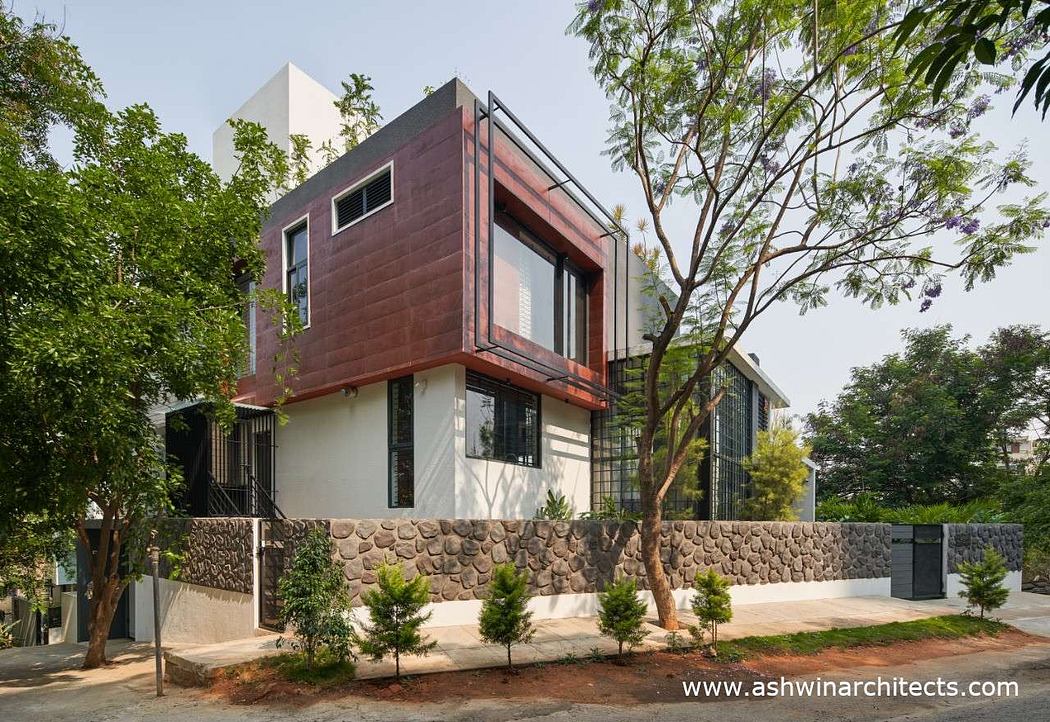 A modern, angular house with a mix of materials, surrounded by lush greenery.