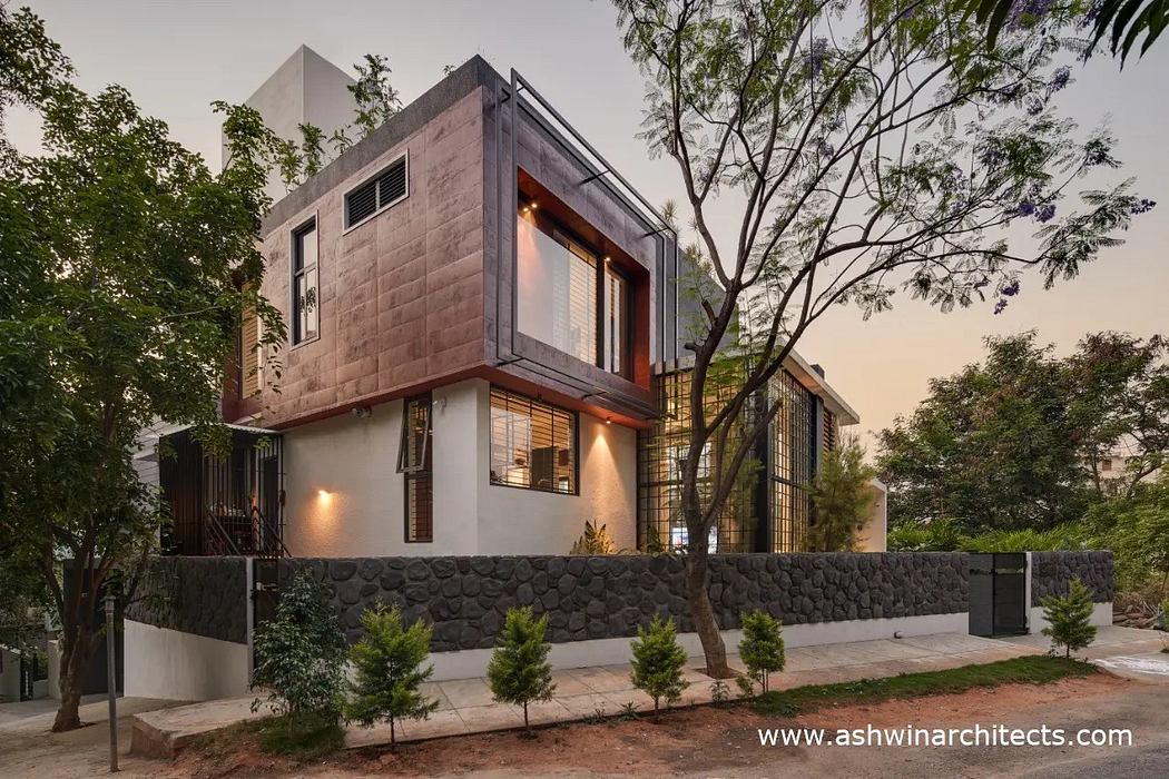 The building features a modern, geometric design with concrete and wood accents, surrounded by lush greenery.