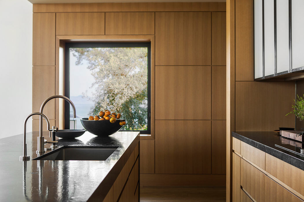 Modern kitchen with sleek wooden cabinetry, large window, and black stone countertop.