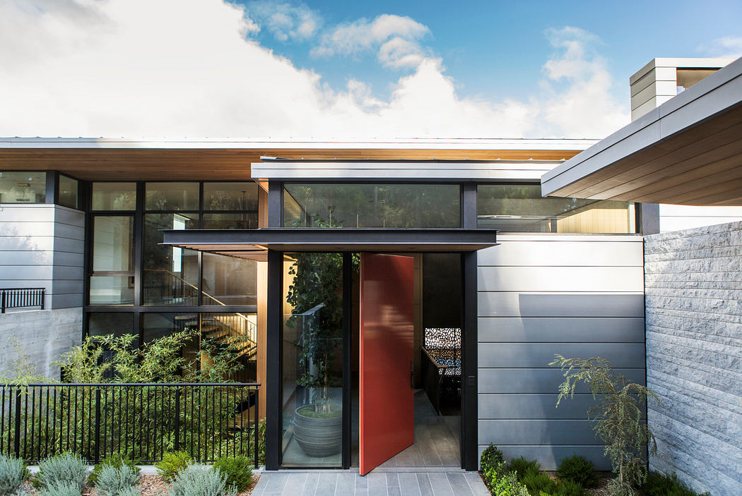 Modern architectural exterior with sleek wood and metal elements, large glass panels, and a bright red entryway.